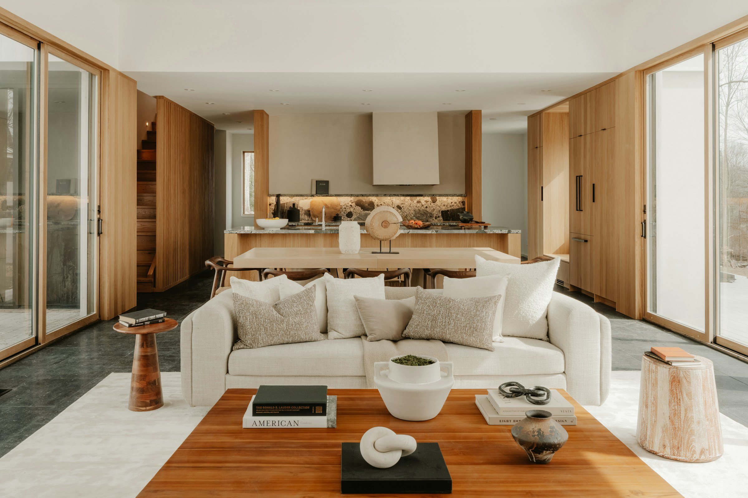 An open living room and kitchen in white oak and plaster, a stone splashback behind the range, a cream sofa, light from both sides