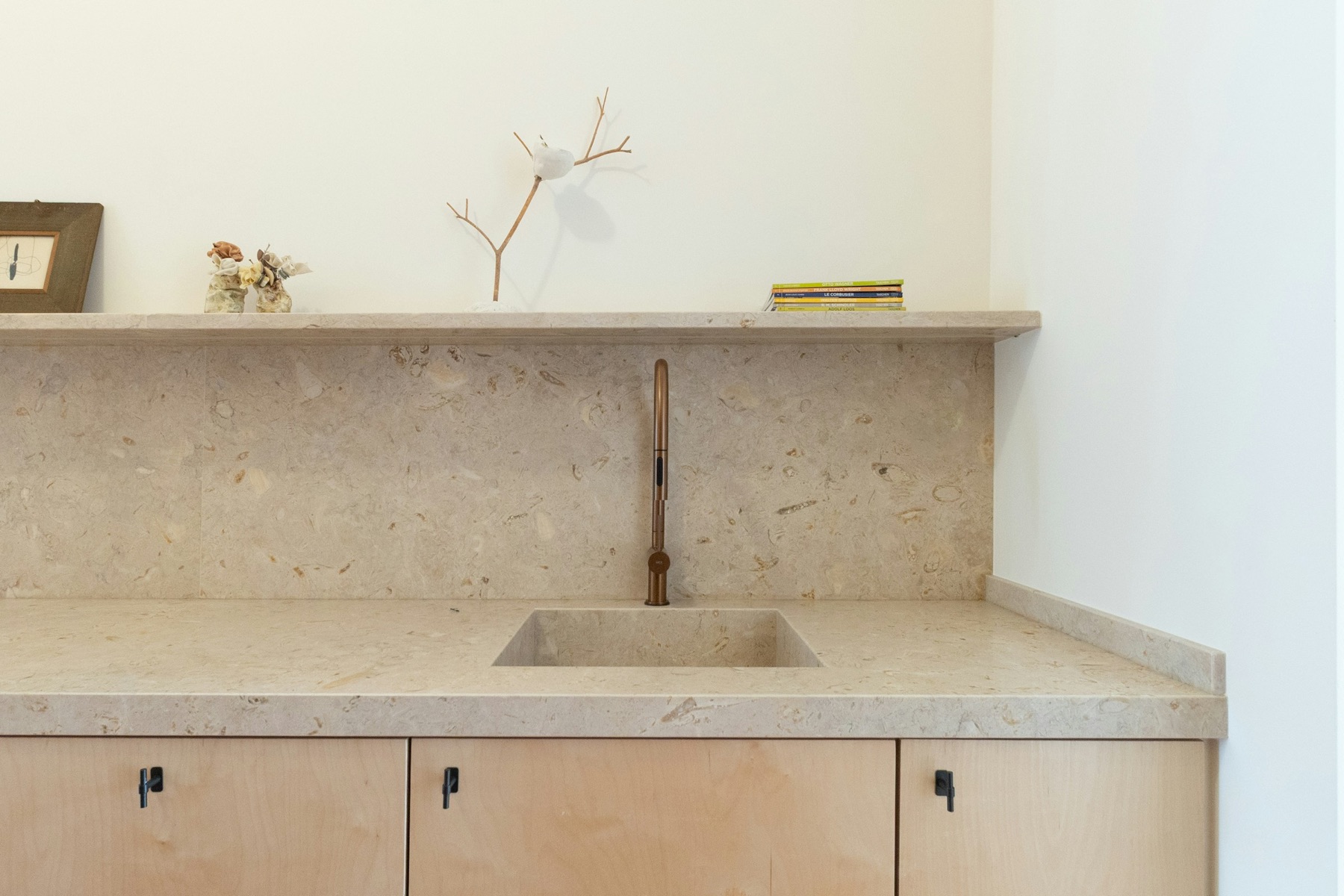A utility sink cut into a pale terrazzo counter, a brass tap against a stone splashback, birch cupboards below