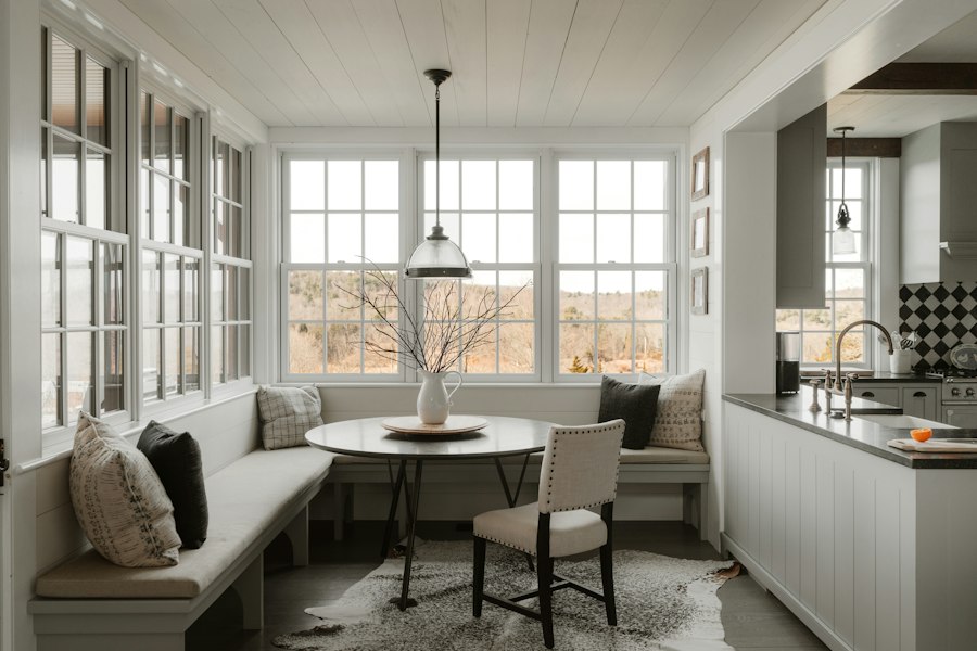 A calm breakfast nook: a built-in banquette, a round table under a glass pendant, tall windows onto winter fields