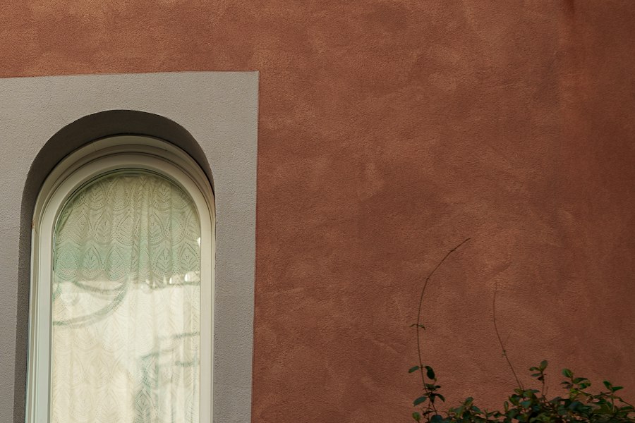 A terracotta lime-plaster wall beside an arched window