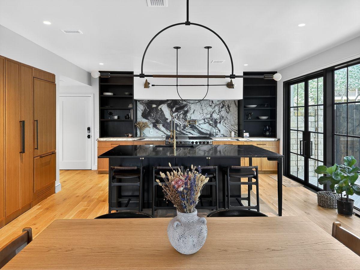 After: a long dining table and a black island kitchen with a marble wall