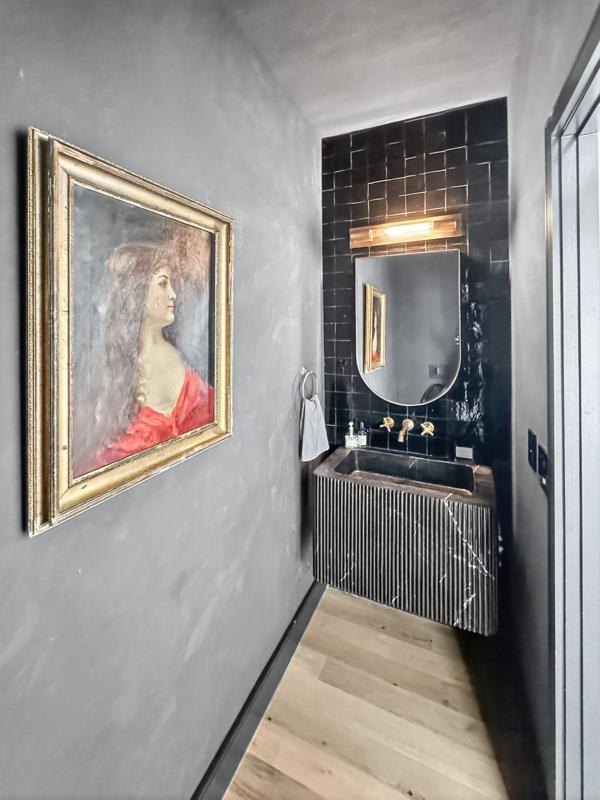 A dark powder room with a stone sink and a portrait