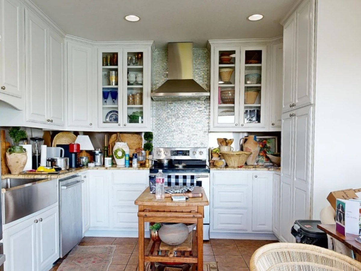 Before: a white kitchen with a steel hood, glass-front cabinets and terracotta tile