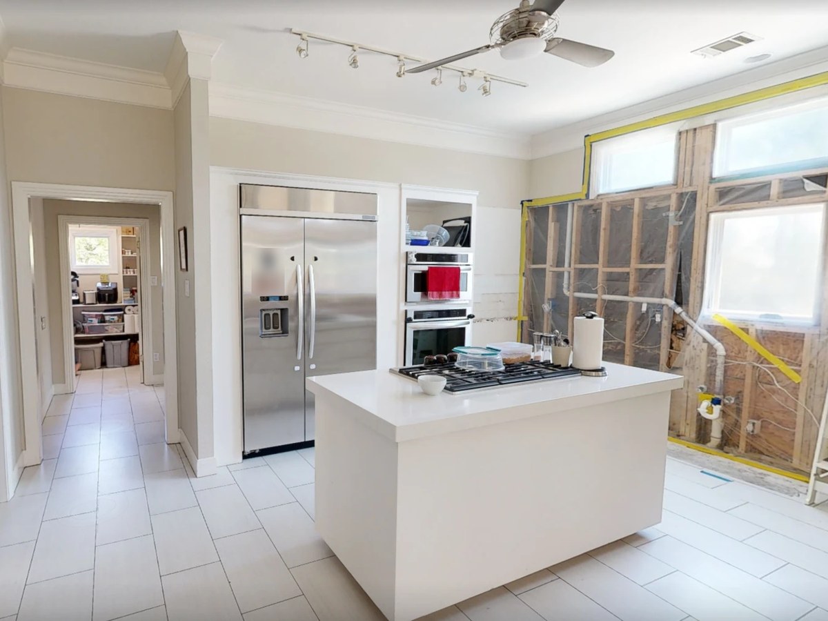 Before: a white kitchen with a steel fridge, its window wall opened to the studs