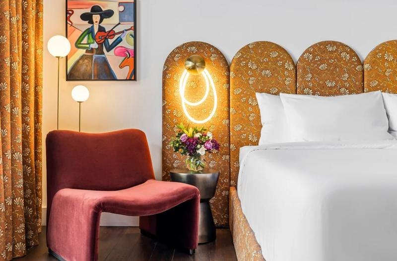 A guest room with a scalloped floral headboard and a red velvet chair