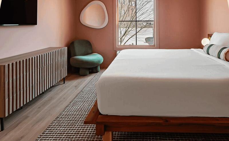 A clay-pink guest room with a low wood bed and a green velvet chair
