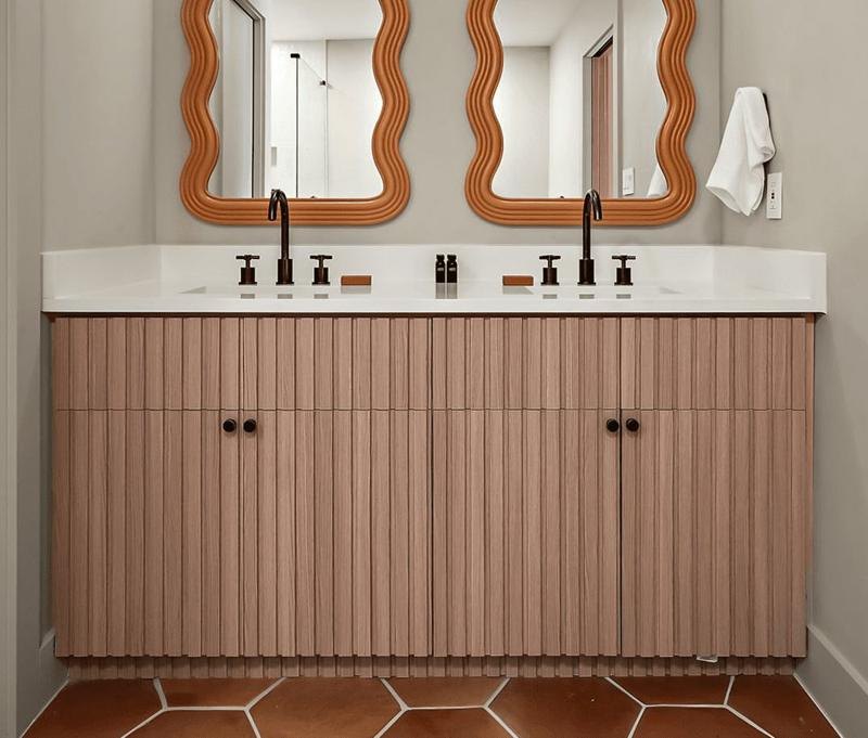 A double vanity with fluted wood doors, wavy terracotta mirrors and hexagon tile