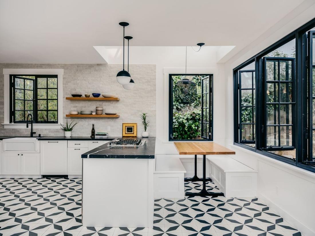 A white kitchen with black steel windows, patterned cement tile and a bench along the window wall