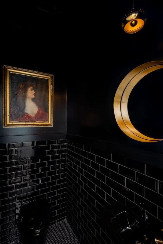 A black powder room with a gold crescent mirror